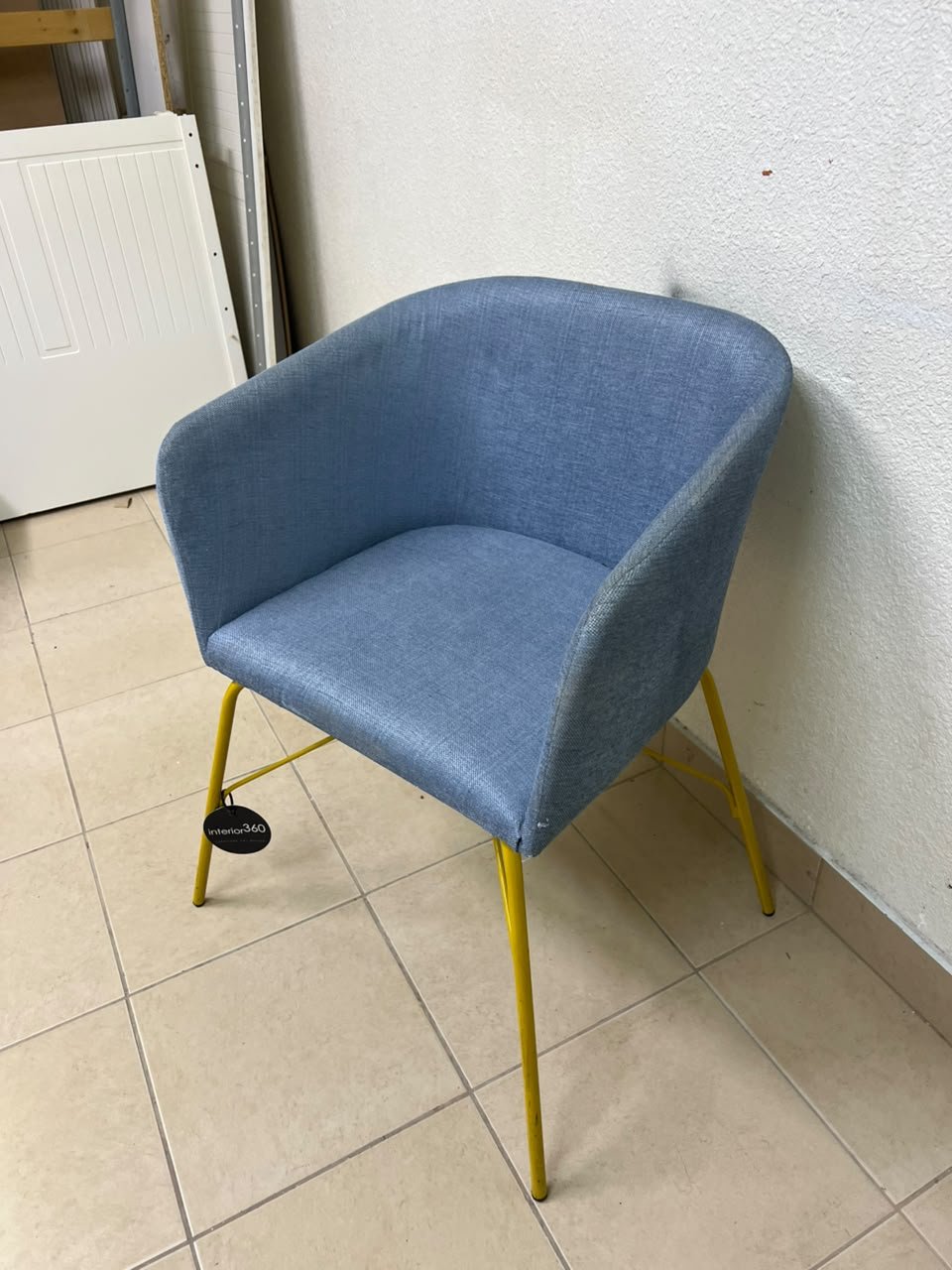 A modern barrel-style armchair or upholstered dining chair, featuring light blue fabric upholstery and slender yellow metal legs. - Image 3