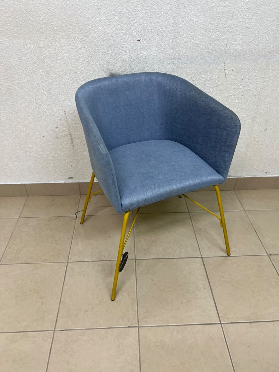 A modern barrel-style armchair or upholstered dining chair, featuring light blue fabric upholstery and slender yellow metal legs.