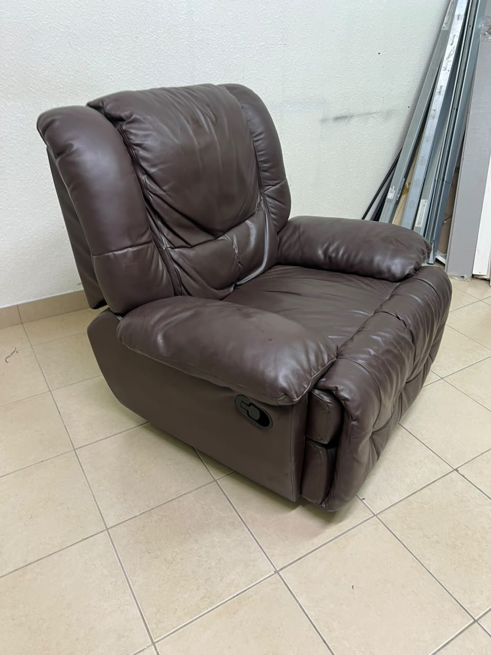 A brown faux leather single recliner featuring padded armrests and backrest, and a manual side handle for position control.