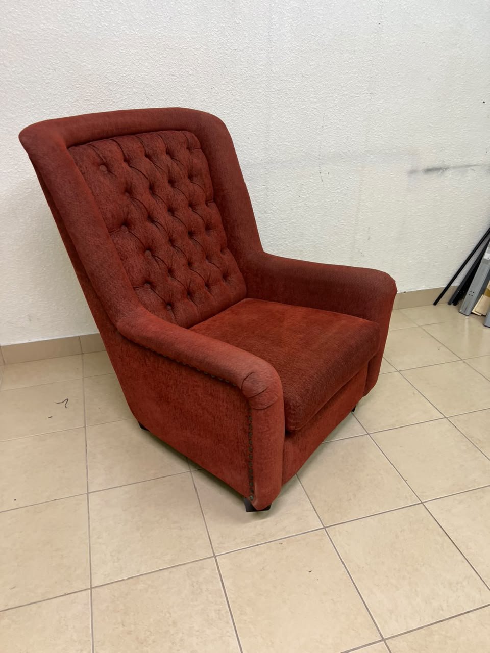 A classic-style armchair featuring a high, button-tufted backrest, upholstered in textured dark red fabric, and accented with metal nailhead trim along the edges.