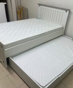 A white wooden single bed featuring a pull-out trundle bed underneath, with two matching padded mattresses.
