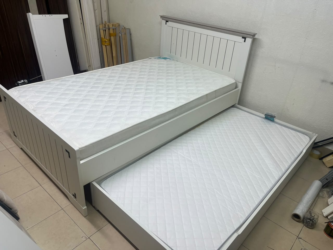 A white wooden single bed featuring a pull-out trundle bed underneath, with two matching padded mattresses. - Image 5