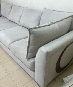 A modern sectional sofa upholstered in light gray fabric, featuring wide armrests with striking rounded details and matching, separate back cushions.