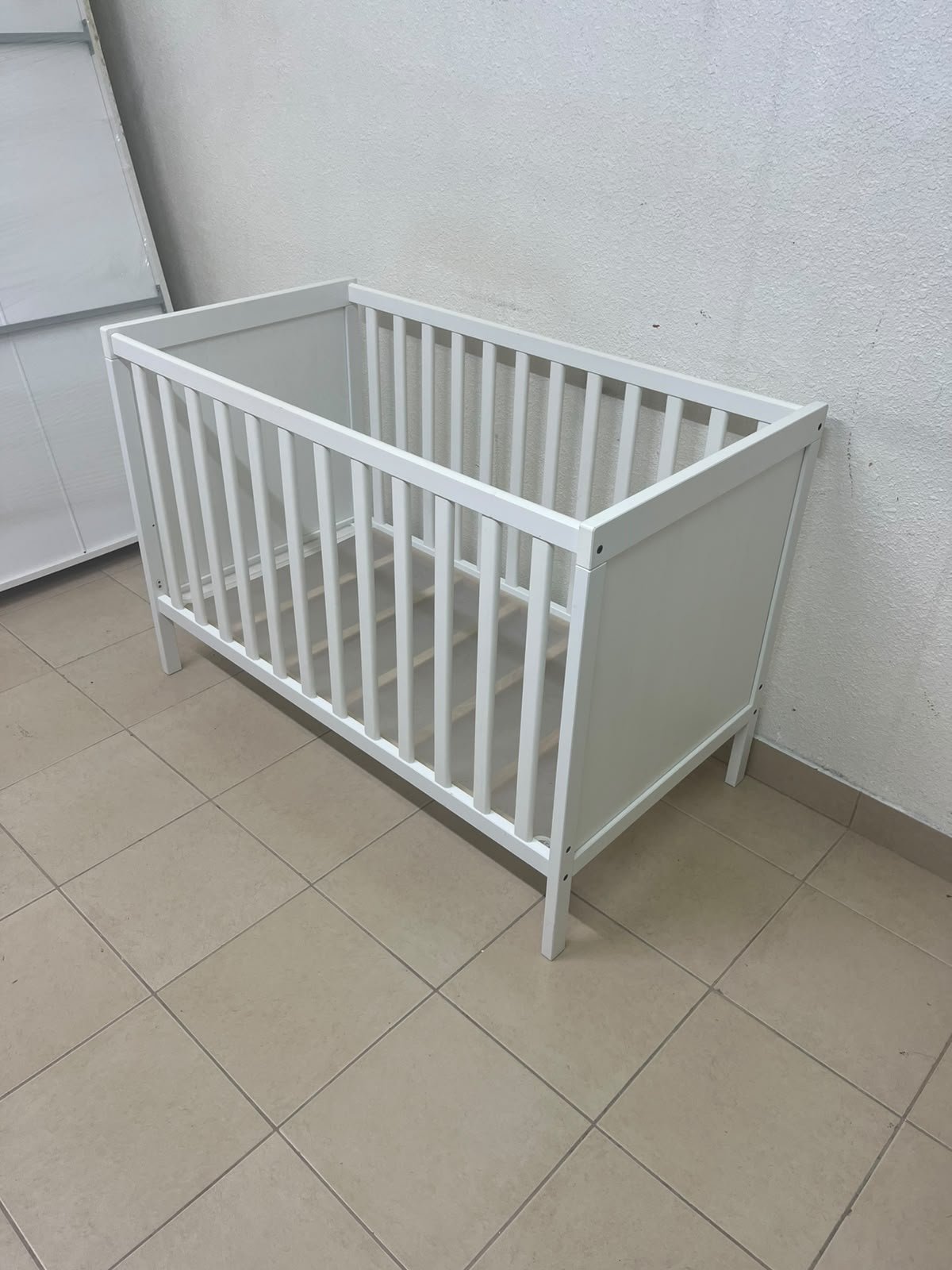 The white IKEA SUNDVIK crib (60x120 cm) features a sturdy wooden design and a bed base that can be adjusted to two different heights. - Image 3