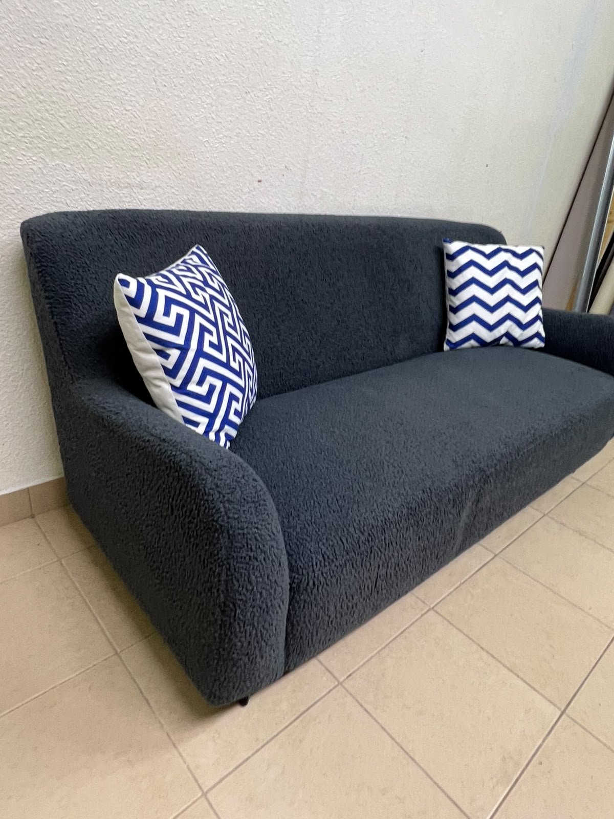 A dark blue, textured fabric sofa, adorned with two decorative cushions featuring patterns that combine blue and white. - Image 2