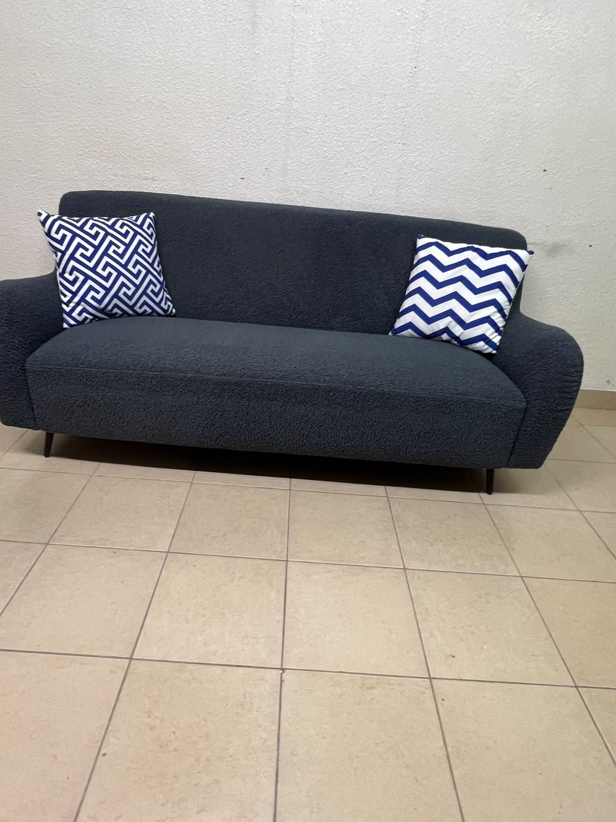 A dark blue, textured fabric sofa, adorned with two decorative cushions featuring patterns that combine blue and white. - Image 3