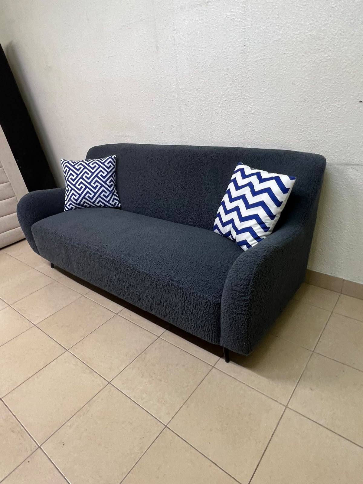 A dark blue, textured fabric sofa, adorned with two decorative cushions featuring patterns that combine blue and white. - Image 4