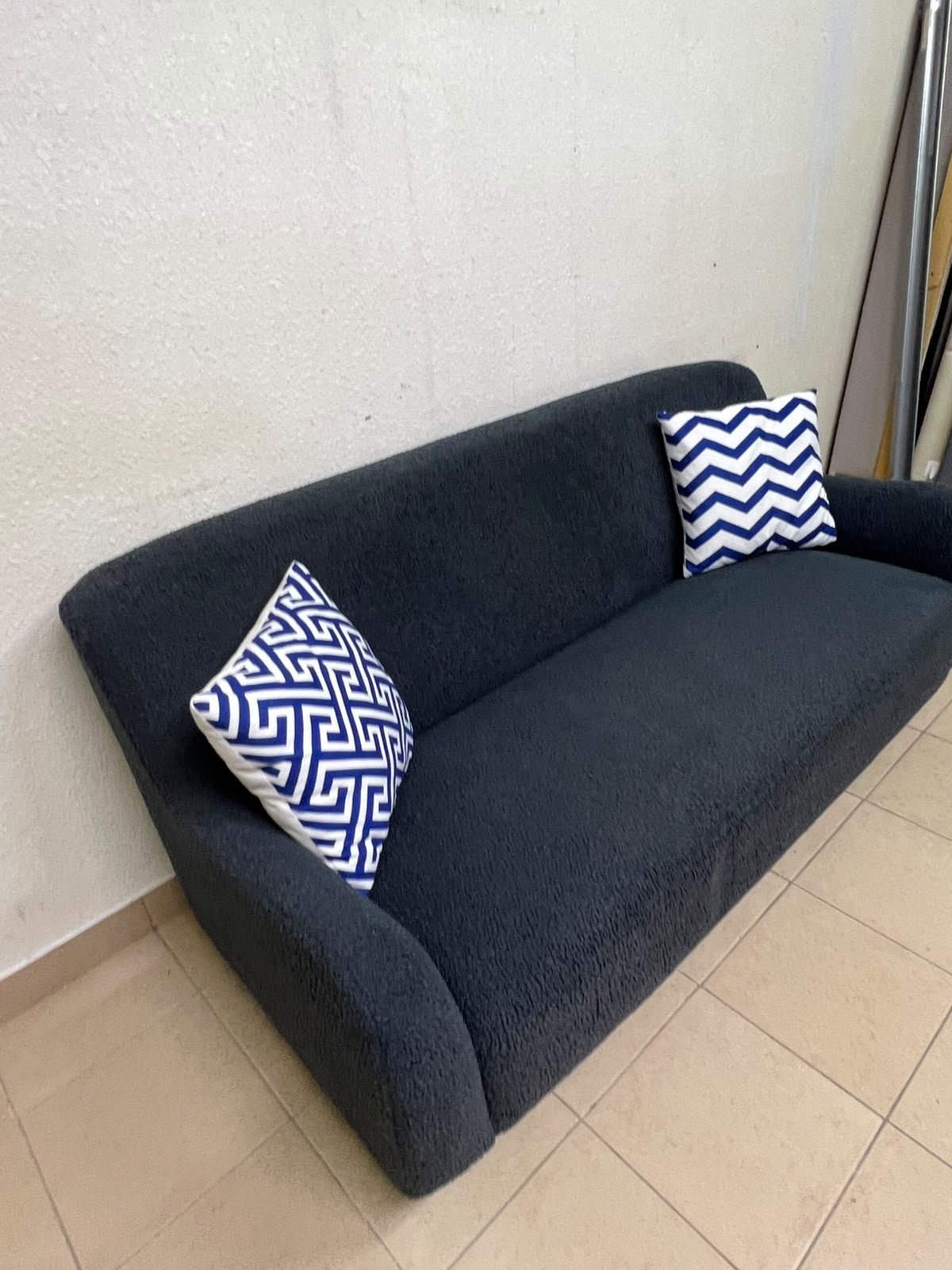 A dark blue, textured fabric sofa, adorned with two decorative cushions featuring patterns that combine blue and white. - Image 5