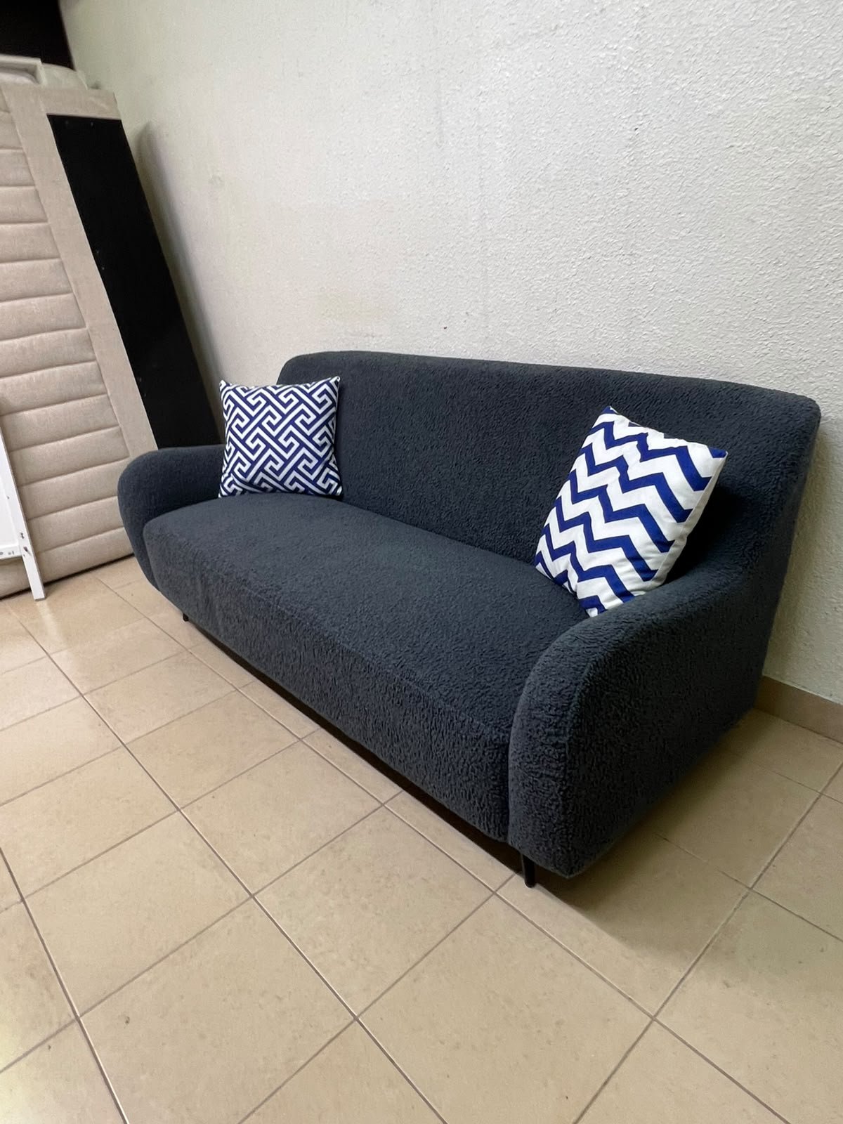 A dark blue, textured fabric sofa, adorned with two decorative cushions featuring patterns that combine blue and white. - Image 9