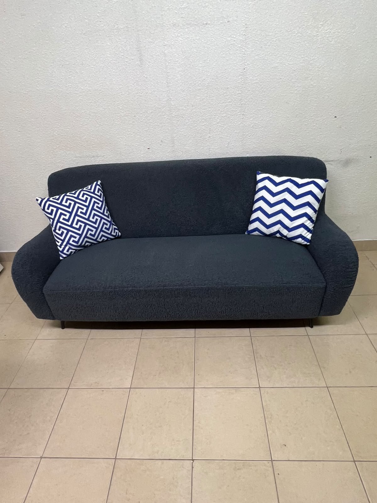 A dark blue, textured fabric sofa, adorned with two decorative cushions featuring patterns that combine blue and white. - Image 8