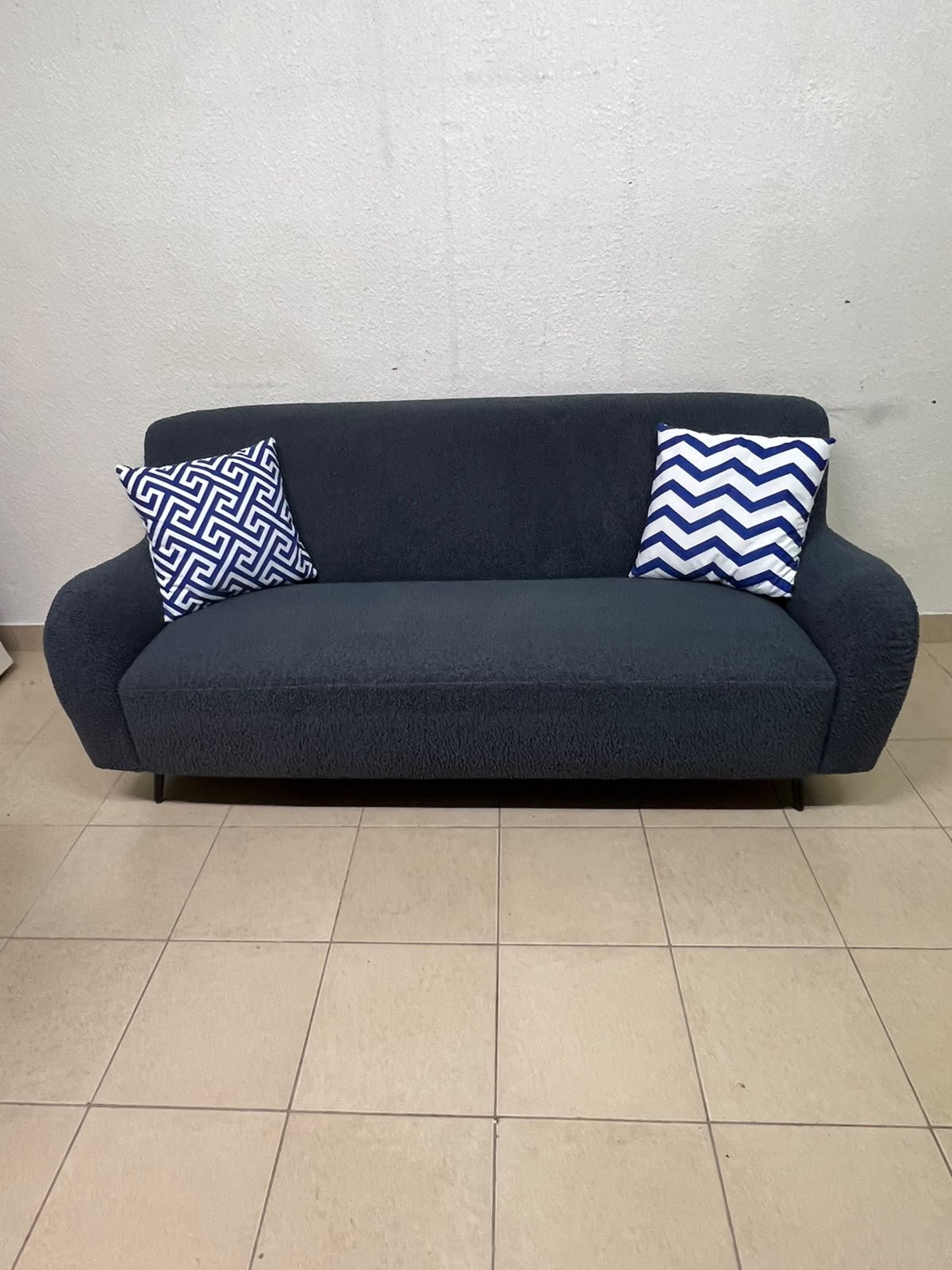A dark blue, textured fabric sofa, adorned with two decorative cushions featuring patterns that combine blue and white. - Image 6