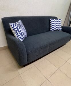 A dark blue, textured fabric sofa, adorned with two decorative cushions featuring patterns that combine blue and white.