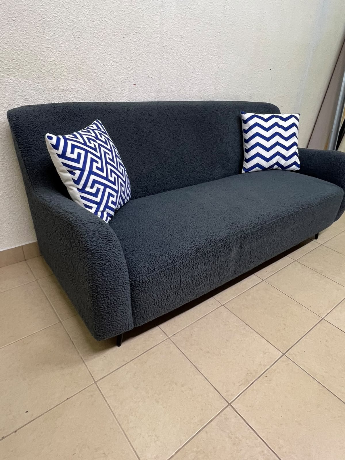 A dark blue, textured fabric sofa, adorned with two decorative cushions featuring patterns that combine blue and white.