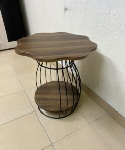This modern two-tier side table features a wooden top with curved edges and a lower storage shelf enclosed by a black metal frame designed like a wire mesh cage.
