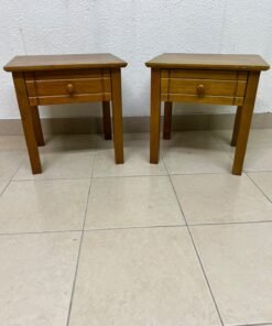 Two classic, medium-toned wooden side tables featuring a single drawer with a round wooden knob and classic grooved detailing on the frame.