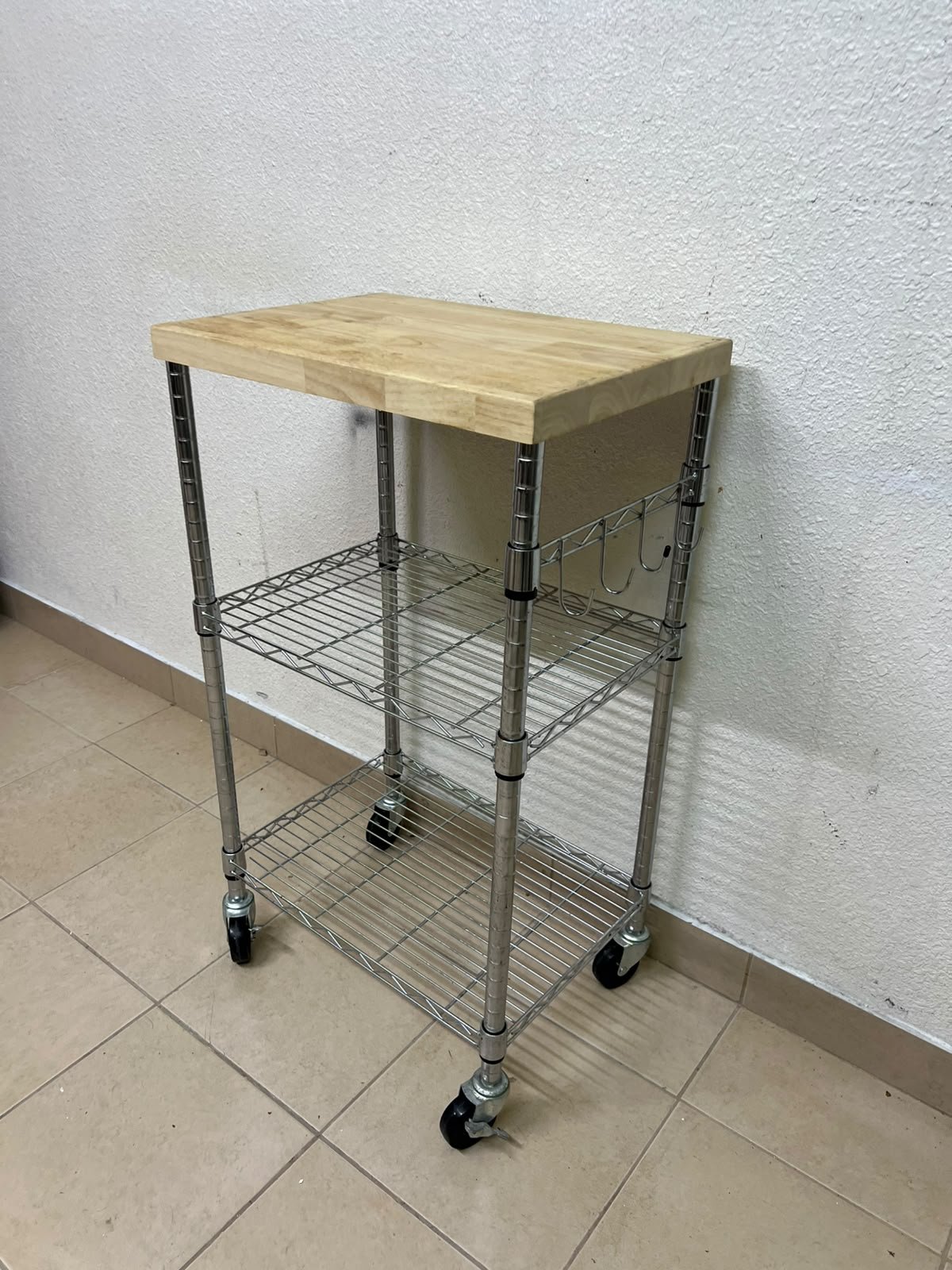 A multi-shelf kitchen cart made of chrome wire, featuring a light-colored wood top (butcher block style) and swivel casters. - Image 3