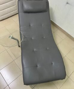 A modern grey faux leather chaise longue featuring an attached round glass side table and metal legs. - Image 3