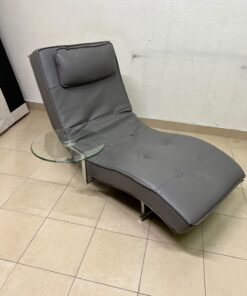 A modern grey faux leather chaise longue featuring an attached round glass side table and metal legs. - Image 4