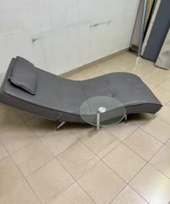 A modern grey faux leather chaise longue featuring an attached round glass side table and metal legs. - Image 6