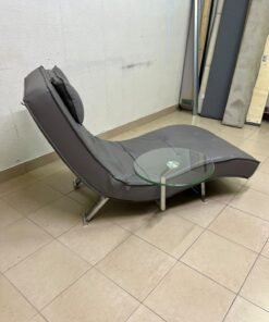 A modern grey faux leather chaise longue featuring an attached round glass side table and metal legs. - Image 7