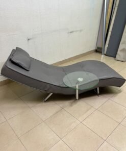 A modern grey faux leather chaise longue featuring an attached round glass side table and metal legs. - Image 8