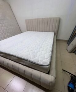 A bed featuring a modern design and a beige upholstered frame, complete with a headboard designed with padded vertical channels and a matching upholstered base; its style resembles the "Curvy Haze" upholstered bed available at Home Box. - Image 2