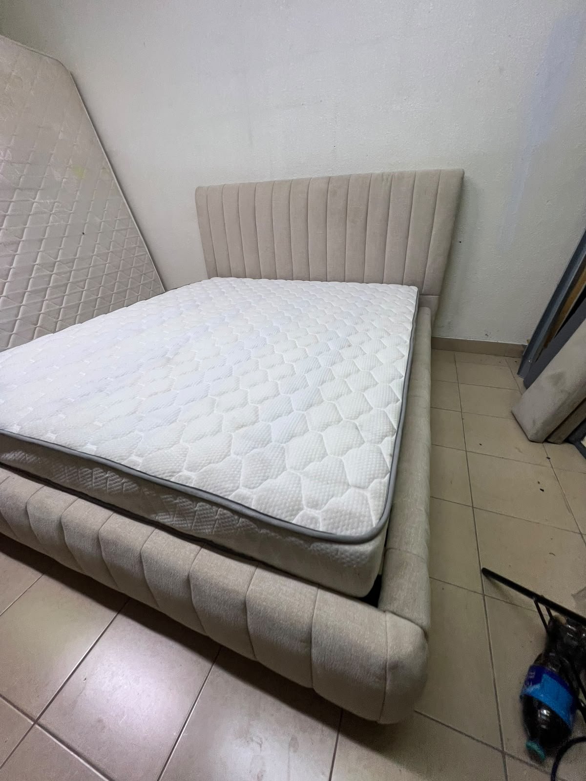 A bed featuring a modern design and a beige upholstered frame, complete with a headboard designed with padded vertical channels and a matching upholstered base; its style resembles the "Curvy Haze" upholstered bed available at Home Box. - Image 2