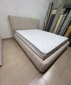 A bed featuring a modern design and a beige upholstered frame, complete with a headboard designed with padded vertical channels and a matching upholstered base; its style resembles the "Curvy Haze" upholstered bed available at Home Box. - Image 3