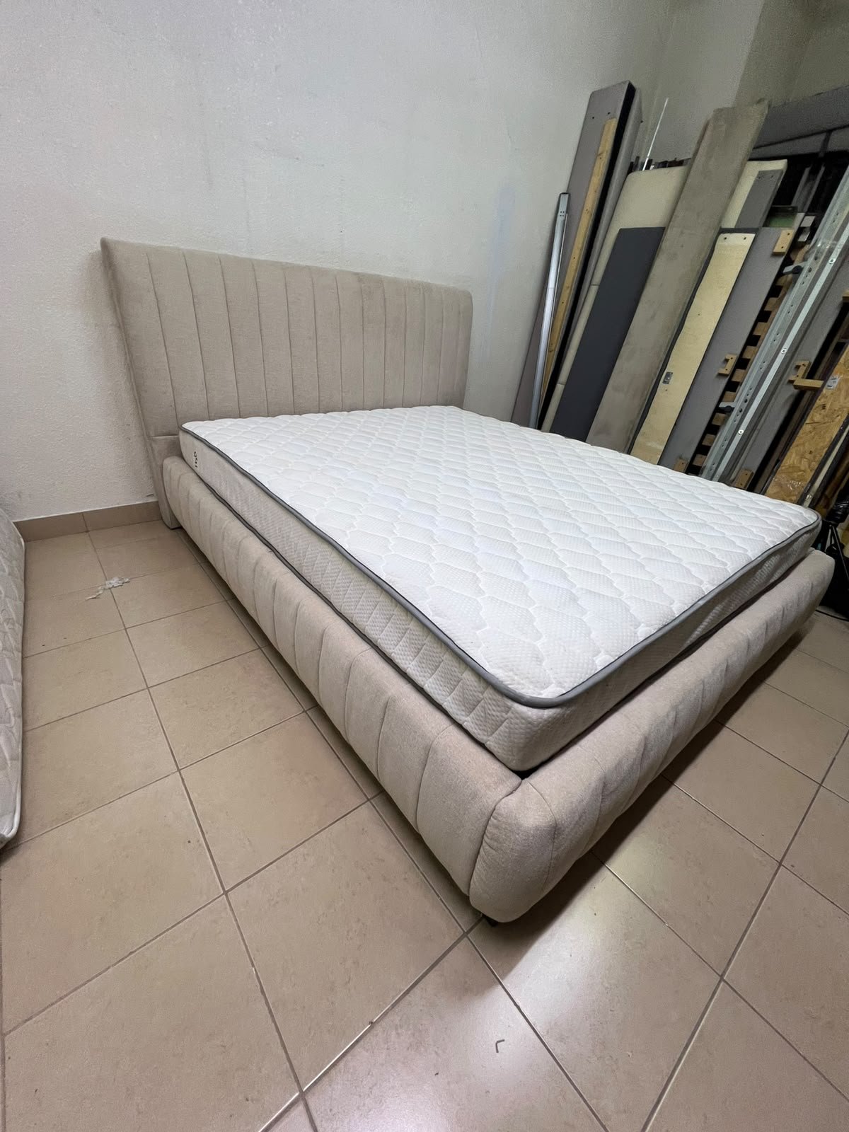 A bed featuring a modern design and a beige upholstered frame, complete with a headboard designed with padded vertical channels and a matching upholstered base; its style resembles the "Curvy Haze" upholstered bed available at Home Box. - Image 3