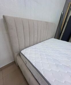 A bed featuring a modern design and a beige upholstered frame, complete with a headboard designed with padded vertical channels and a matching upholstered base; its style resembles the "Curvy Haze" upholstered bed available at Home Box. - Image 4