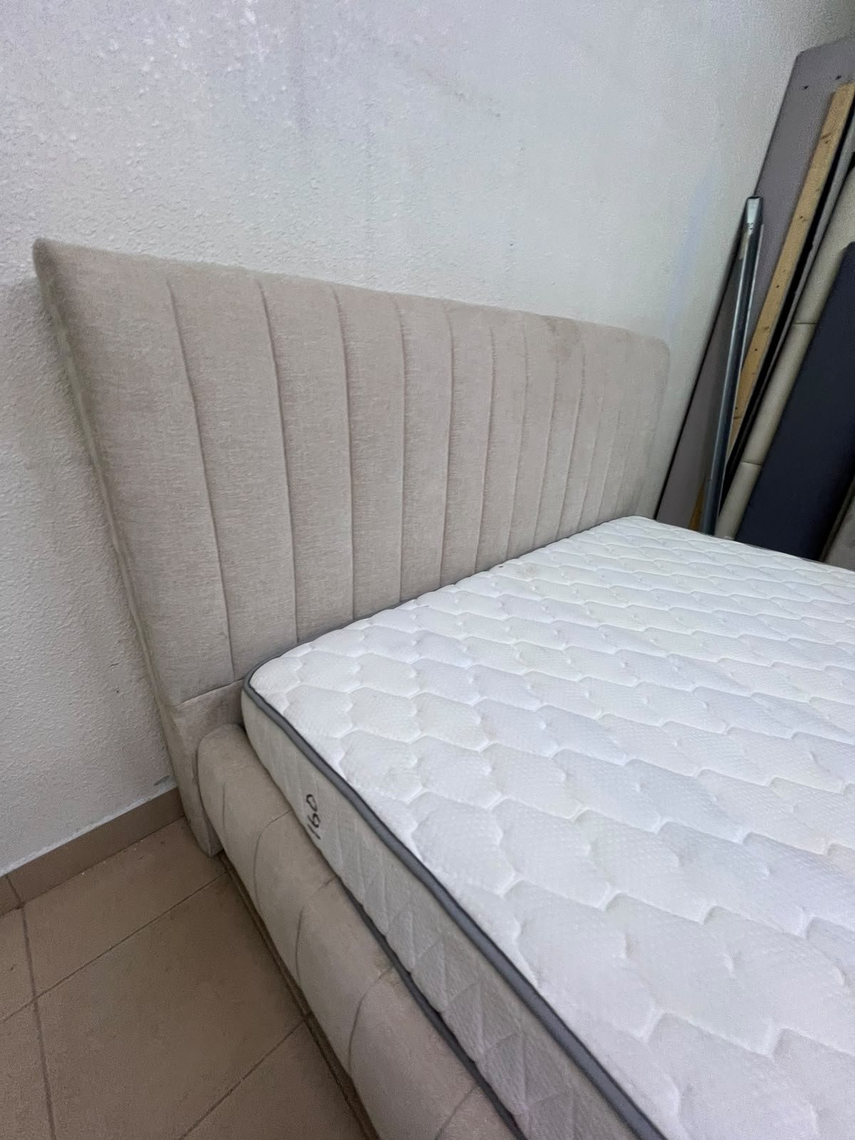 A bed featuring a modern design and a beige upholstered frame, complete with a headboard designed with padded vertical channels and a matching upholstered base; its style resembles the "Curvy Haze" upholstered bed available at Home Box. - Image 4
