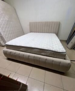A bed featuring a modern design and a beige upholstered frame, complete with a headboard designed with padded vertical channels and a matching upholstered base; its style resembles the "Curvy Haze" upholstered bed available at Home Box. - Image 5