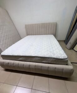 A bed featuring a modern design and a beige upholstered frame, complete with a headboard designed with padded vertical channels and a matching upholstered base; its style resembles the "Curvy Haze" upholstered bed available at Home Box. - Image 6