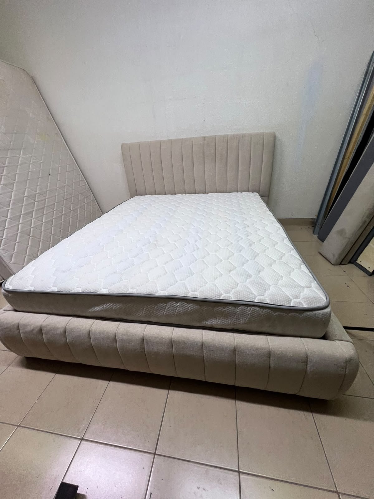 A bed featuring a modern design and a beige upholstered frame, complete with a headboard designed with padded vertical channels and a matching upholstered base; its style resembles the "Curvy Haze" upholstered bed available at Home Box. - Image 6