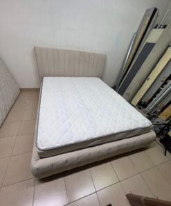 A bed featuring a modern design and a beige upholstered frame, complete with a headboard designed with padded vertical channels and a matching upholstered base; its style resembles the "Curvy Haze" upholstered bed available at Home Box. - Image 9