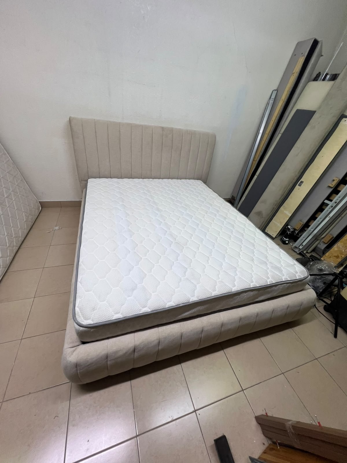 A bed featuring a modern design and a beige upholstered frame, complete with a headboard designed with padded vertical channels and a matching upholstered base; its style resembles the "Curvy Haze" upholstered bed available at Home Box. - Image 9