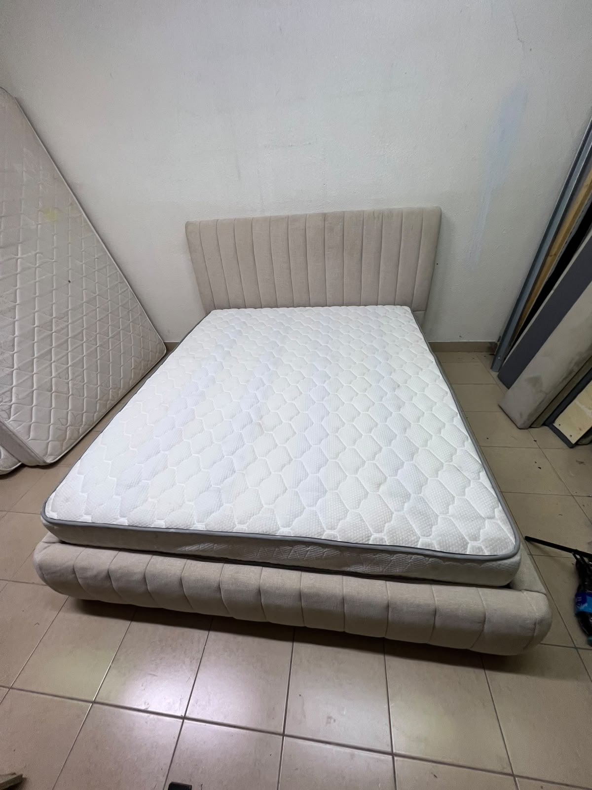 A bed featuring a modern design and a beige upholstered frame, complete with a headboard designed with padded vertical channels and a matching upholstered base; its style resembles the "Curvy Haze" upholstered bed available at Home Box. - Image 10