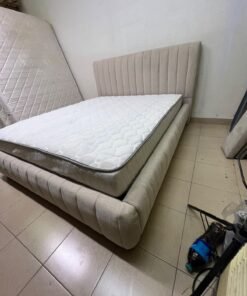 A bed featuring a modern design and a beige upholstered frame, complete with a headboard designed with padded vertical channels and a matching upholstered base; its style resembles the "Curvy Haze" upholstered bed available at Home Box. - Image 11