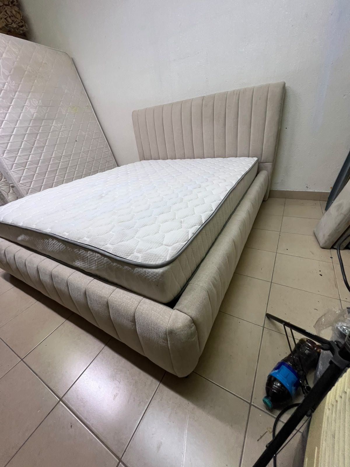 A bed featuring a modern design and a beige upholstered frame, complete with a headboard designed with padded vertical channels and a matching upholstered base; its style resembles the "Curvy Haze" upholstered bed available at Home Box. - Image 11