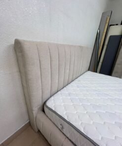 A bed featuring a modern design and a beige upholstered frame, complete with a headboard designed with padded vertical channels and a matching upholstered base; its style resembles the "Curvy Haze" upholstered bed available at Home Box. - Image 12