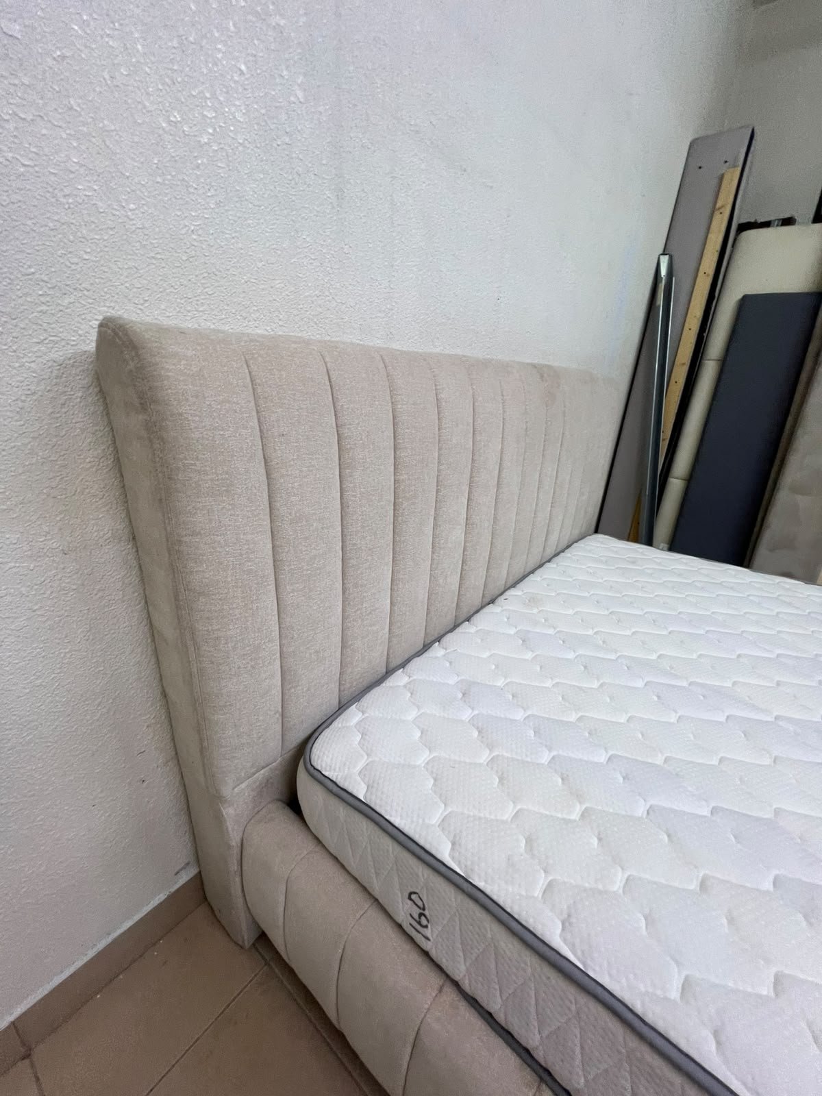 A bed featuring a modern design and a beige upholstered frame, complete with a headboard designed with padded vertical channels and a matching upholstered base; its style resembles the "Curvy Haze" upholstered bed available at Home Box. - Image 12
