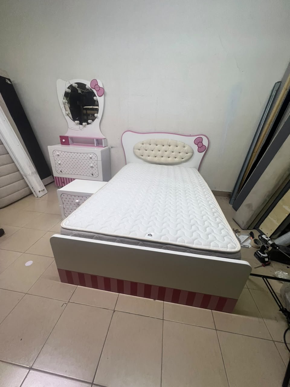 A girls' bedroom featuring a white and pink color scheme, including a bed with bedding, a storage table with an illuminated mirror, and a bedside table. - Image 12