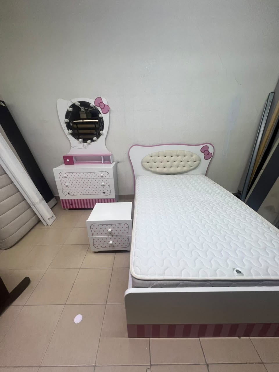 A girls' bedroom featuring a white and pink color scheme, including a bed with bedding, a storage table with an illuminated mirror, and a bedside table. - Image 2