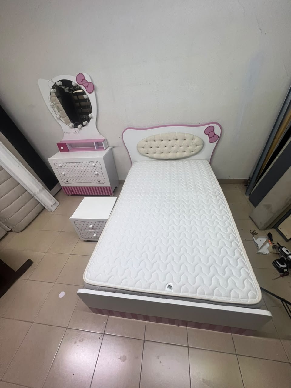 A girls' bedroom featuring a white and pink color scheme, including a bed with bedding, a storage table with an illuminated mirror, and a bedside table. - Image 4