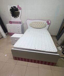 A girls' bedroom featuring a white and pink color scheme, including a bed with bedding, a storage table with an illuminated mirror, and a bedside table.