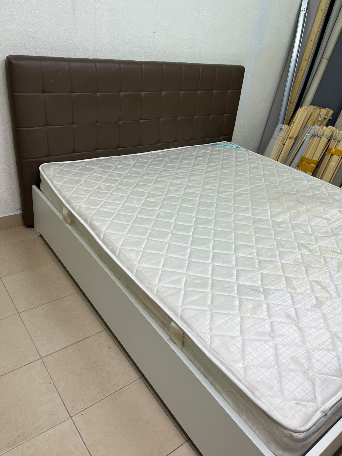 A modern white wooden king-size bed, paired with a cushioned spring mattress and a brown faux-leather upholstered headboard.