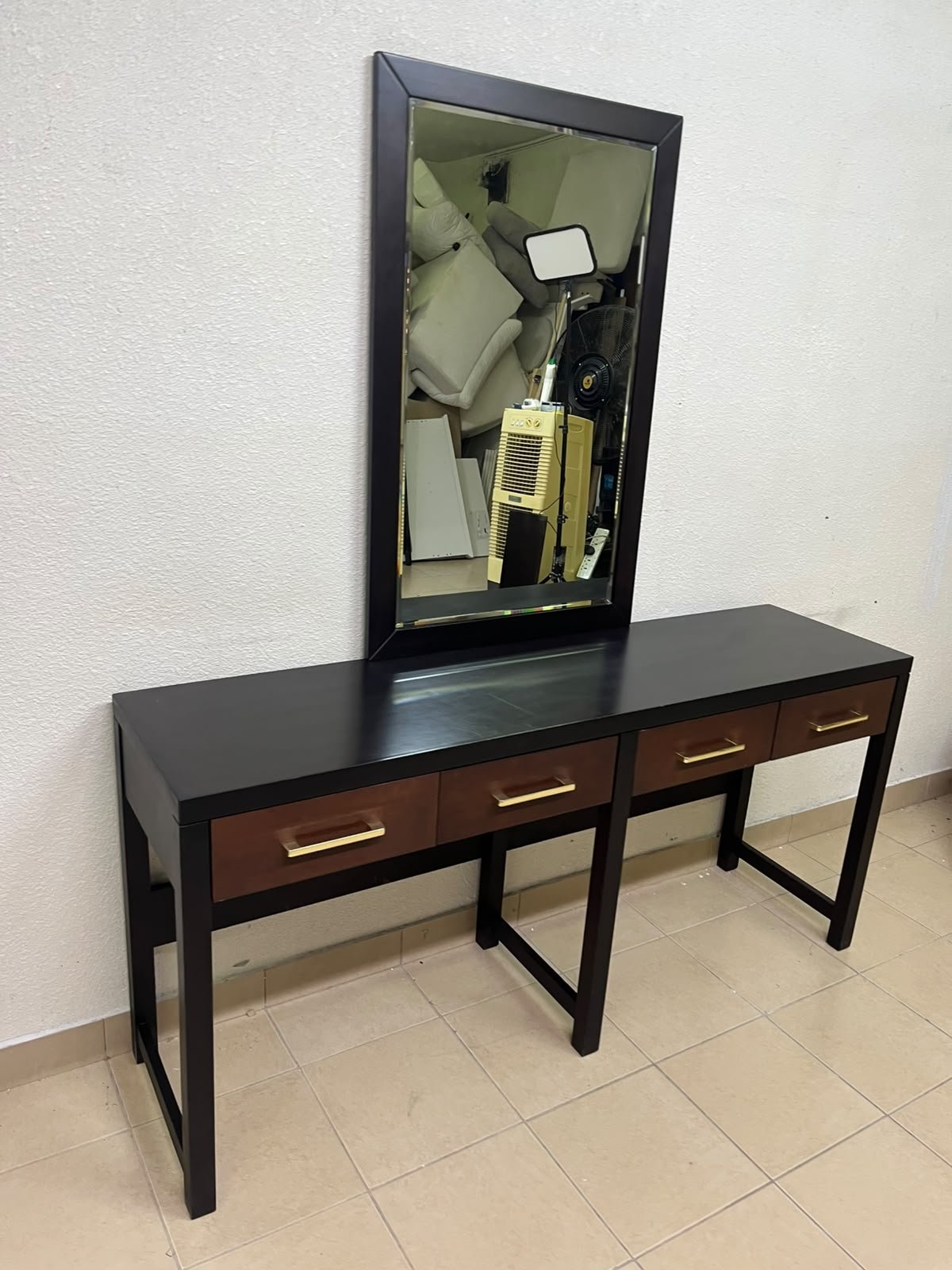 An ultra-long, modern console or vanity table featuring a black wooden frame, contrasting warm-toned wooden drawers, and gold-finished metal handles; it comes with a matching wall mirror.
