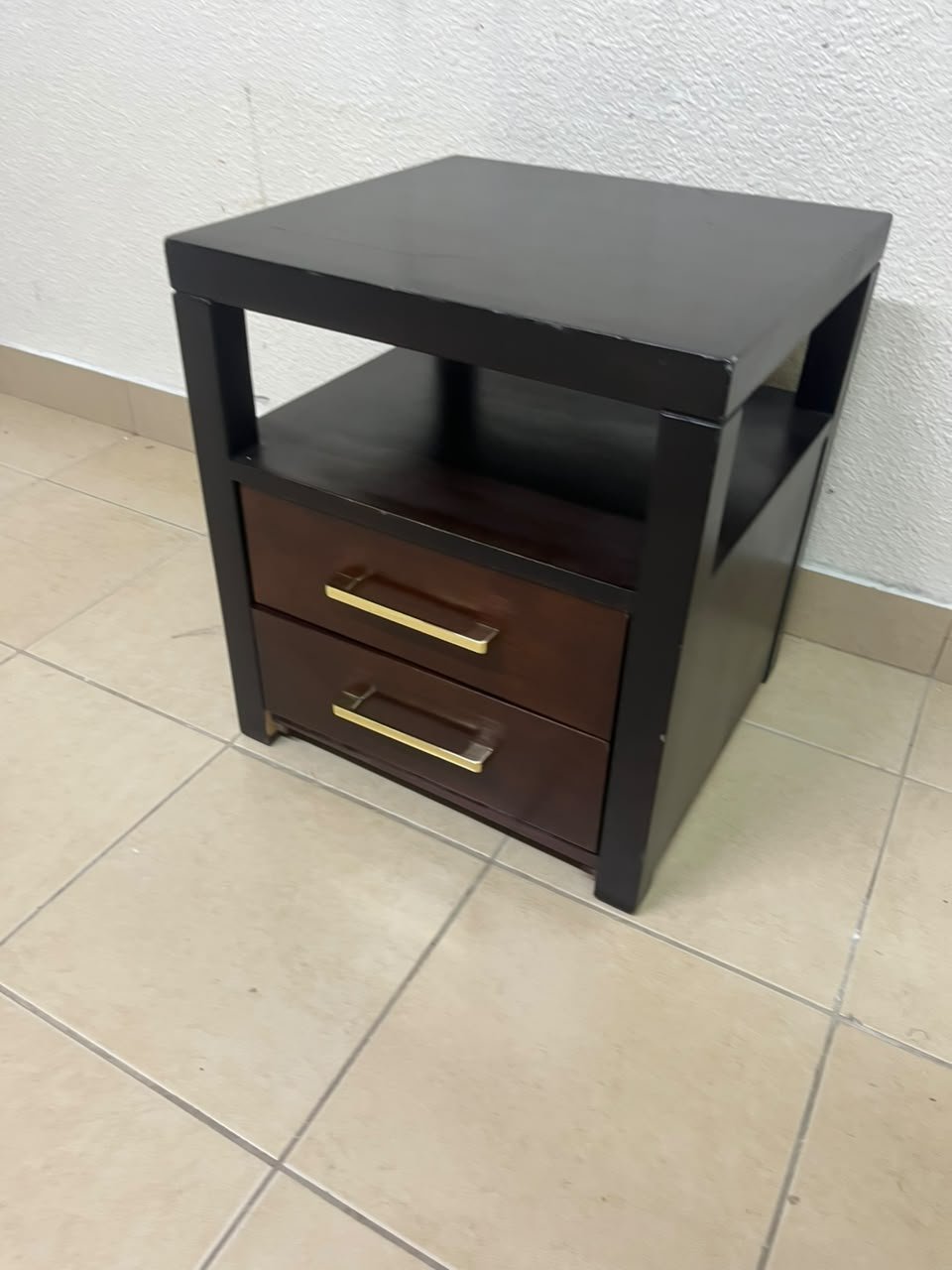 A modern wooden side table featuring two drawers and an open shelf, with a dark wood frame that contrasts with the reddish-brown drawer fronts, accented by slender metal handles.