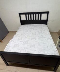 An IKEA "HEMNES" wooden bed frame in a black-brown finish, featuring a slatted headboard and a matching mattress.