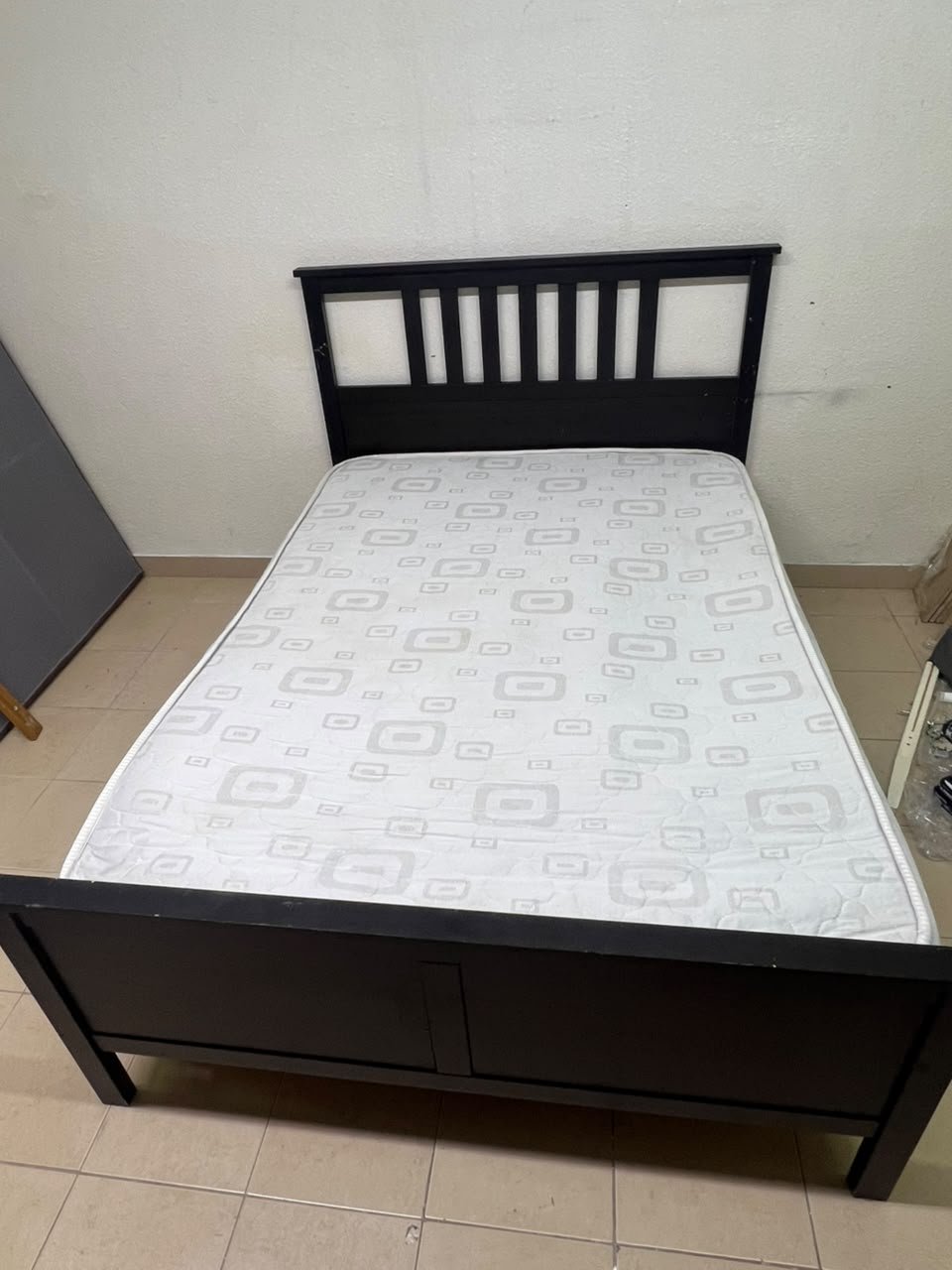 An IKEA "HEMNES" wooden bed frame in a black-brown finish, featuring a slatted headboard and a matching mattress.